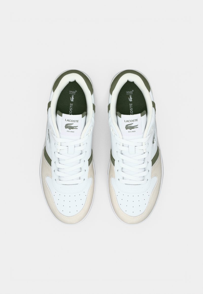 Paire de baskets blanches Lacoste avec accents beige et vert, bout perforé, et languette à logo, vues de dessus sur un fond uni.