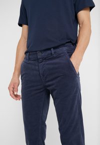 Laivastonsiniset samettihousut, joissa on kapeahko leikkaus, napillinen kiinnitys, etutaskut ja hienovarainen ribbikuvio. Yhdistetty tumman t-paidan kanssa.