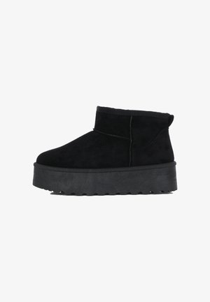 Botas de tobillo de ante negro con corte bajo, forma redondeada y suelas de goma negra gruesa y texturizada con un patrón de relieve.
