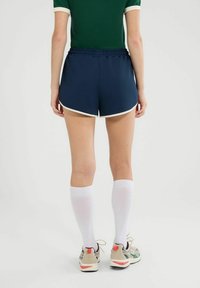 Marineblauwe sportshorts met witte accenten, voorzien van een elastische tailleband. Draag ze met knielange witte sokken en beige sportschoenen.