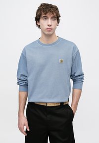 Φορμα παντελονιού από βαμβάκι ανοιχτού γαλάζιου χρώματος με μακριά μανίκια, ριμπ μανσέτες και μικρό κεντημένο λογότυπο εμπρός, συνδυασμένο με μαύρο παντελόνι.