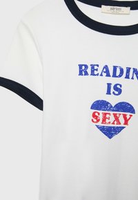 Bílý tričko s námořnickým modrým límcem a okraji rukávů. Obsahuje výrazný, otrhaný text: "ČTENÍ JE SEXY" v modré a červené barvě, s modrým srdcem.