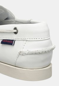 Scarpa da barca in pelle bianca con design cucito, dotata di suola in gomma e un piccolo logo Sebago rosso e blu sul lato.