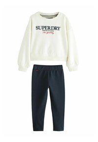 Kremeni dukserica s "SUPERDRY" logom, u kombinaciji s tamnoplave tajice. Mekani pamučni materijal, opušten kroj, rebrasti rukavi i pojas.