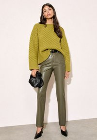 Olīvzaļš adīts džemperis ar teksturētu rakstu, apvienots ar pieguļošām olīvzaļām mākslīgās ādas biksēm. Melna sajūga soma un melni apavi ar izteiktu purngalu pabeidz izskatu.