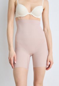 Yksinkertaiset, pehmeästä ja joustavasta kankaasta valmistetut korkeavyötäröiset muotoilevat shortsit, joissa on sileä nude-väri ja polven ylle ulottuva pituus saumattomalla muotoilulla.
