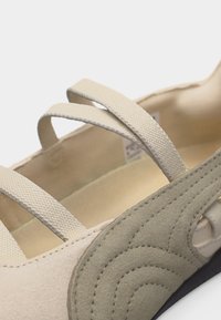 Sandale beige clair avec trois lanières texturées et un détail de couture en suède sur le côté près du talon élastique.