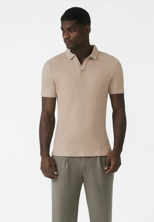 Tricou polo bej cu dungi, croială slim, mâneci scurte și guler clasic. Asortat cu pantaloni plisati gri deschis. Textură netedă.