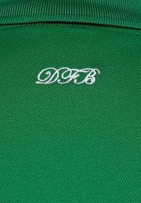 Tissu vert avec une surface texturée et un col côtelé, affichant en évidence les lettres brodées blanches "DFB".