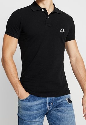 Zwart poloshirt van katoen, met een knoopsluiting met twee knopen en een klein geborduurd logo op de linkerborst, gecombineerd met blauwe beschadigde jeans.