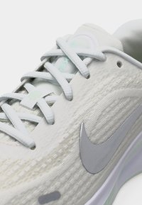 Κοντινό πλάνο λευκού αθλητικού παπουτσιού με υφασμάτινη υφή, λευκά κορδόνια και γκρι λογότυπο Nike στο πλάι.