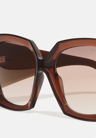 Brown oversized sunglasses with a geometric frame, gradient lenses, and a glossy finish. Features a prominent thick temple and angular corners.
