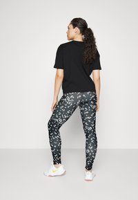 T-shirt preto de mangas curtas, ajustado, combinado com leggings de cintura alta apresentando um padrão de manchas cinzas e brancas. Sapatos brancos com detalhes amarelos.