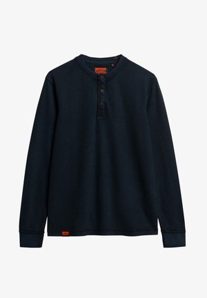 Camisa henley de manga larga en azul marino oscuro con un acabado texturizado, tapeta de tres botones y parche con logo en el dobladillo. Corte clásico con puños acanalados.