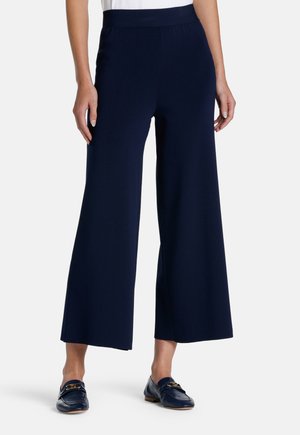 Pantaloni a gamba larga di colore navy con una texture liscia, vita elastica e vestibilità rilassata, abbinati a mocassini navy con un accento decorativo in metallo.
