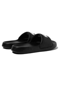 Black slide sandals with a smooth surface, wide straps, and a textured footbed. Features a white logo on one strap and the brand name embossed.