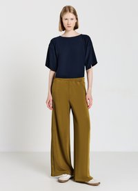 Maglietta oversized blu navy con maniche ampie abbinata a pantaloni larghi verde oliva con bottoni laterali, progettata per il comfort. Sneakers bianche.