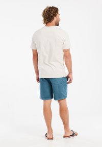 Cremefarvet bomulds t-shirt og blå shorts, begge med afslappet pasform. Shortsene har sidelommer og en glat tekstur, og sandaler fuldender outfittet.