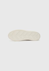 Sola di una sneaker realizzata in gomma, di colore bianco con un motivo di battistrada testurizzato per la presa, caratterizzata da un bordo liscio e dettagli di branding.