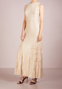 Beige spets maxiklänning med en figursydd bodice, rundad halsringning och lager av volanger i nederkanten. Matchad med svarta, remmar på högklackade sandaler.