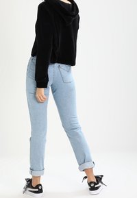 Schwarze, gekürzte Samthoodie, hellblaue, umgeschlagene Jeans und schwarze Sneakers mit weißen Akzenten und Logo. Einfaches, legeres Outfit.