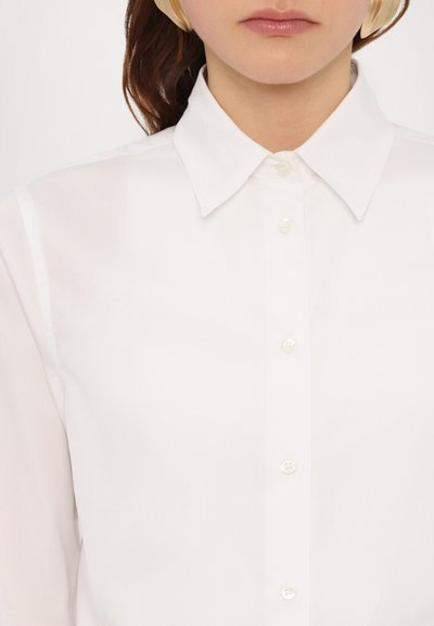 Chemise blanche à col classique, fabriquée dans un mélange de coton lisse. Présente un éclat subtil et six boutons nacrés sur le devant.