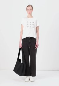 T-shirt bianca con motivi grafici neri, jeans neri a vita alta e una grande borsa a tracolla in pelle nera.