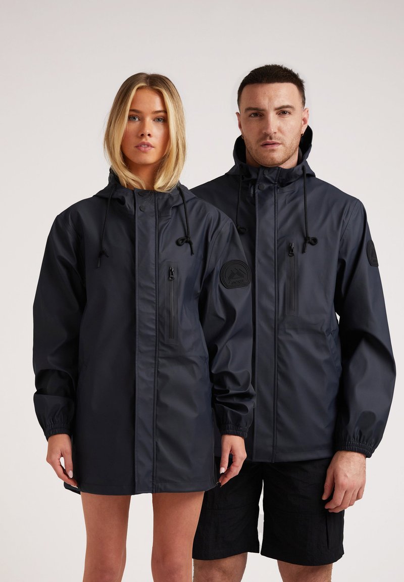 Vestes imperméables marine pour adultes, dotées d'une capuche, de poches zippées et de poignets élastiques, avec un emblème de la marque texturé sur la manche.