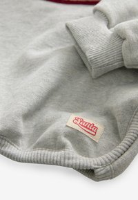 Szary sweatshirt wykonany z miękkiego materiału, z prążkowanymi mankietami i małą kremową metką z czerwonym napisem "Santa" na dolnej krawędzi.