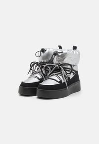 High-top sneakers featuring a shiny silver material and black suede accents, with thick black sole and grey laces. Drawstring top for adjustability.