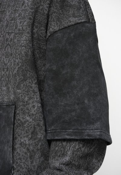 Krupni plan tamnosive uzorkovane jakne s crnim laktom i vidljivim detaljima šivanja.
