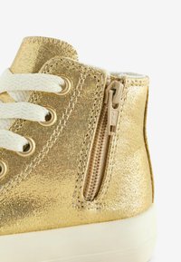 Złote metaliczne sneakersy wysokie z teksturowanej tkaniny, białymi sznurówkami i detalem w postaci bocznego zamka. Posiadają kremową podeszwę.