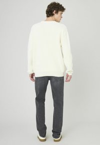 Pull en maille blanc cassé avec texture côtelée, associé à un jean gris. Le pull présente une coupe décontractée et une finition au niveau des hanches. Chaussures décontractées incluses.