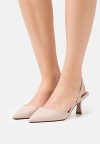 Béžové slingback podpatky s špičatými špičkami, hladký syntetický materiál, nízký blokový podpatek a jemné texturované detaily na pásku.