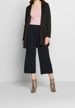 Un lungo blazer nero, un top aderente rosa e pantaloni a gamba larga blu navy abbinati a stivaletti alla caviglia in stampa serpente marrone. Texture lisce e design moderno.