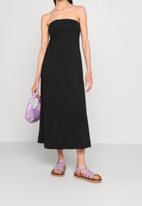 Svart strapless maxikjol med en figursydd överdel och ett flödande kjol. Kombinerad med lavendelfärgade sandaler med remmar och en matchande lila handväska.