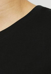 Sort bomulds T-shirt med rund halsudskæring og blød tekstur. Nærbillede viser en glat overflade og veldefineret syning langs kraven.