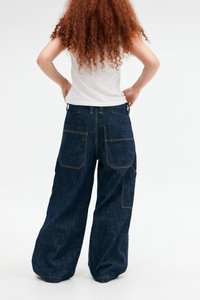 Jeans in denim scuro a gamba larga con cuciture arancioni a contrasto, grandi tasche posteriori e vita pulita, mostrati da dietro.