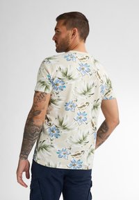 Korte mouwen t-shirt van stof met een lichtbeige achtergrond en blauwe bloem- en groene bladerenpatronen. Standaard ronde halsontwerp.