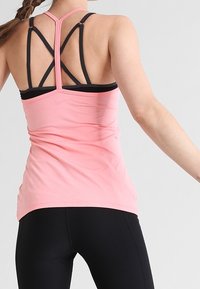 Light pink athletic tank top with a racerback design featuring black straps. The fabric is smooth with a fitted silhouette.