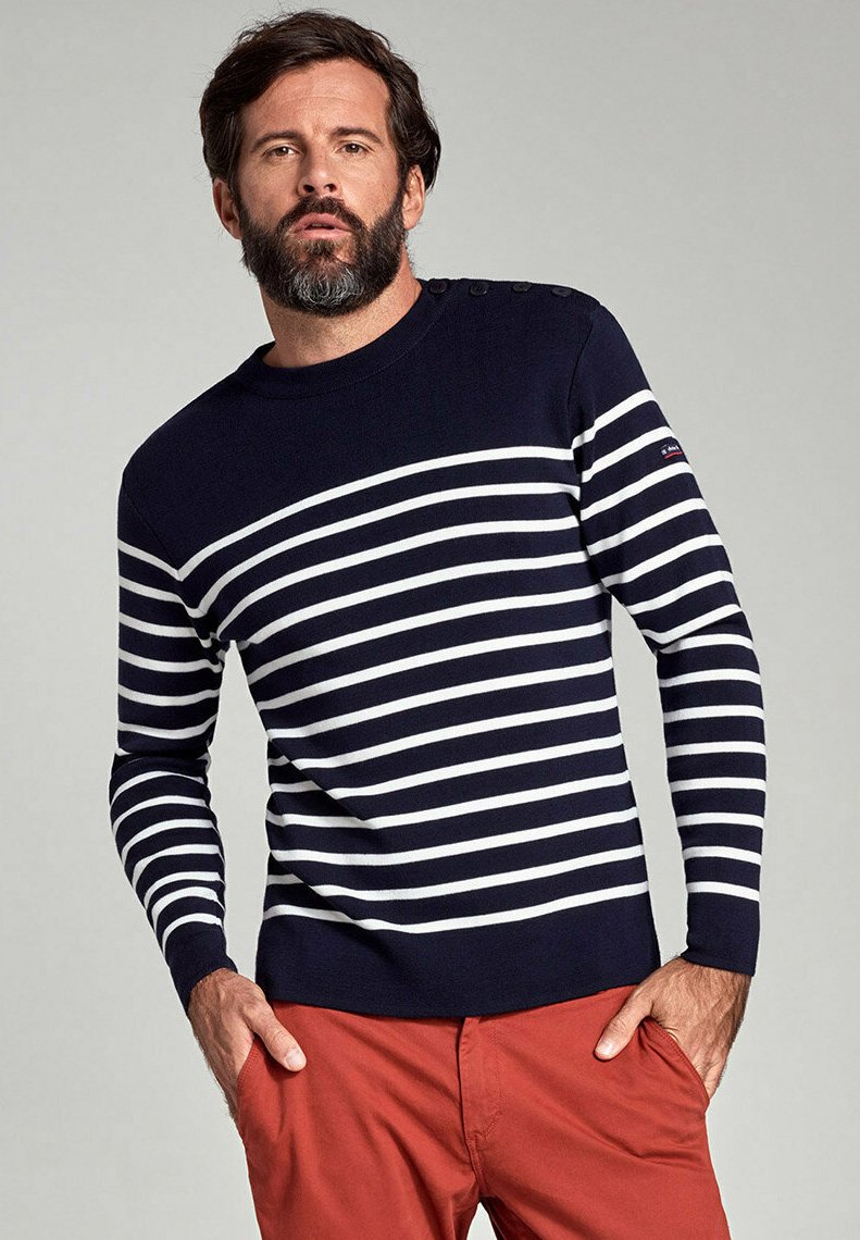Pullover a righe blu navy e bianche con scollo rotondo, maniche lunghe, dettagli con bottoni sulle spalle, indossato con pantaloni rossi.
