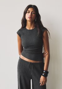 Top en tricot côtelé gris avec des manches courtes, associé à un pantalon ample assorti. Accessoirisé avec des bracelets noirs. Texture lisse, design décontracté.