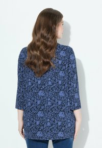 Blouse marine avec un motif floral dans des tons de bleu, à manches trois quarts et à coupe décontractée. Tissu lisse avec une texture douce.