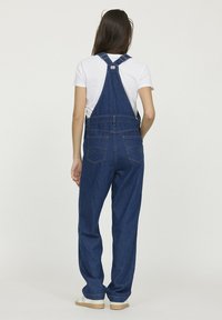 Salopette en denim de couleur bleu foncé, avec des bretelles réglables, une coupe décontractée et deux poches arrière avec des détails de couture visibles.