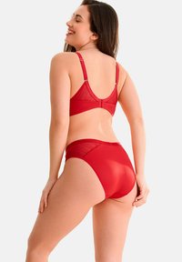 Ensemble de lingerie rouge comprenant un soutien-gorge avec un panneau en maille transparente et des culottes taille haute, mettant en valeur un tissu doux et des bretelles réglables.
