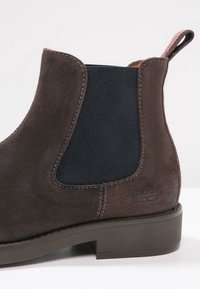 Donkerbruine suède enkelboots met elastische zijkanten en een gestructureerde afwerking, met een vlakke rubberen zool en subtiele logodetail.