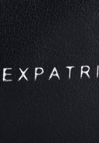 Surface noire texturée avec des lettres blanches en relief formant le mot "EXPATRI" en majuscules.