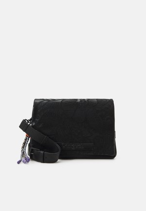 Sac bandoulière noir avec des motifs floraux en relief, une bandoulière ajustable et des pompons tressés multicolores suspendus sur le côté.