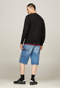 Sudadera negra con puños acanalados, combinada con pantalones cortos cargo de mezclilla azul claro que cuentan con bolsillos laterales y un ajuste relajado. Zapatillas negras y calcetines.
