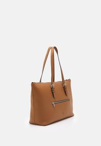 Sac fourre-tout en cuir brun avec deux poignées, surface texturée, poche zippée argentée sur le devant et coutures lisses.